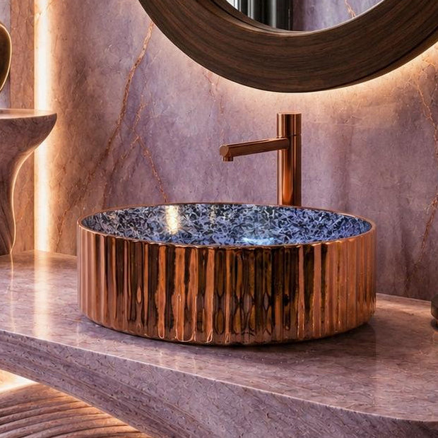 A luxurious bathroom vanity featuring a sculptural wavy stone countertop and matching stone wall and floor, with a copper-toned vessel sink, round mirror, and decorative accessories.