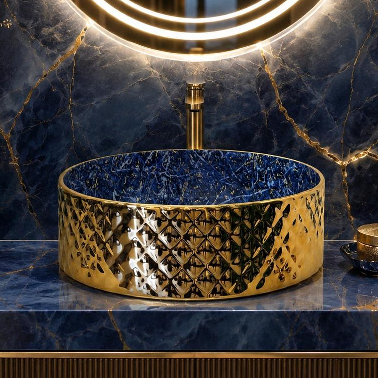 A luxury bathroom vanity setup featuring a round gold vessel sink with a textured diamond pattern, set into a blue marble countertop and matching backsplash. A large illuminated LED ring mirror hangs above, with decorative gold and black vases on either side.