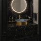 A luxury bathroom vanity featuring a black marble countertop and matching marble backsplash with a glowing circular LED mirror. A gold-finished vessel sink with a blue marbled interior sits on the counter, flanked by gold fixtures.