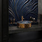 A luxury bathroom vanity setup featuring a hammered gold vessel sink on a dark stone countertop, set against a dramatic dark blue and gold textured wave-patterned backsplash.