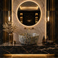 Luxury bathroom vanity featuring a round vessel sink with a black, gold, and white marbled pattern, set on a dark marble countertop with gold accents, a large round backlit mirror, and wall sconces.