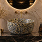 Luxury bathroom vanity featuring a round backlit mirror, a speckled gold and black vessel sink, and dark marble surfaces with gold accents.
